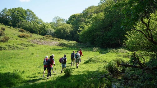 Looking down on a group of walkers walking across the middle of the field with trees on the right hand side